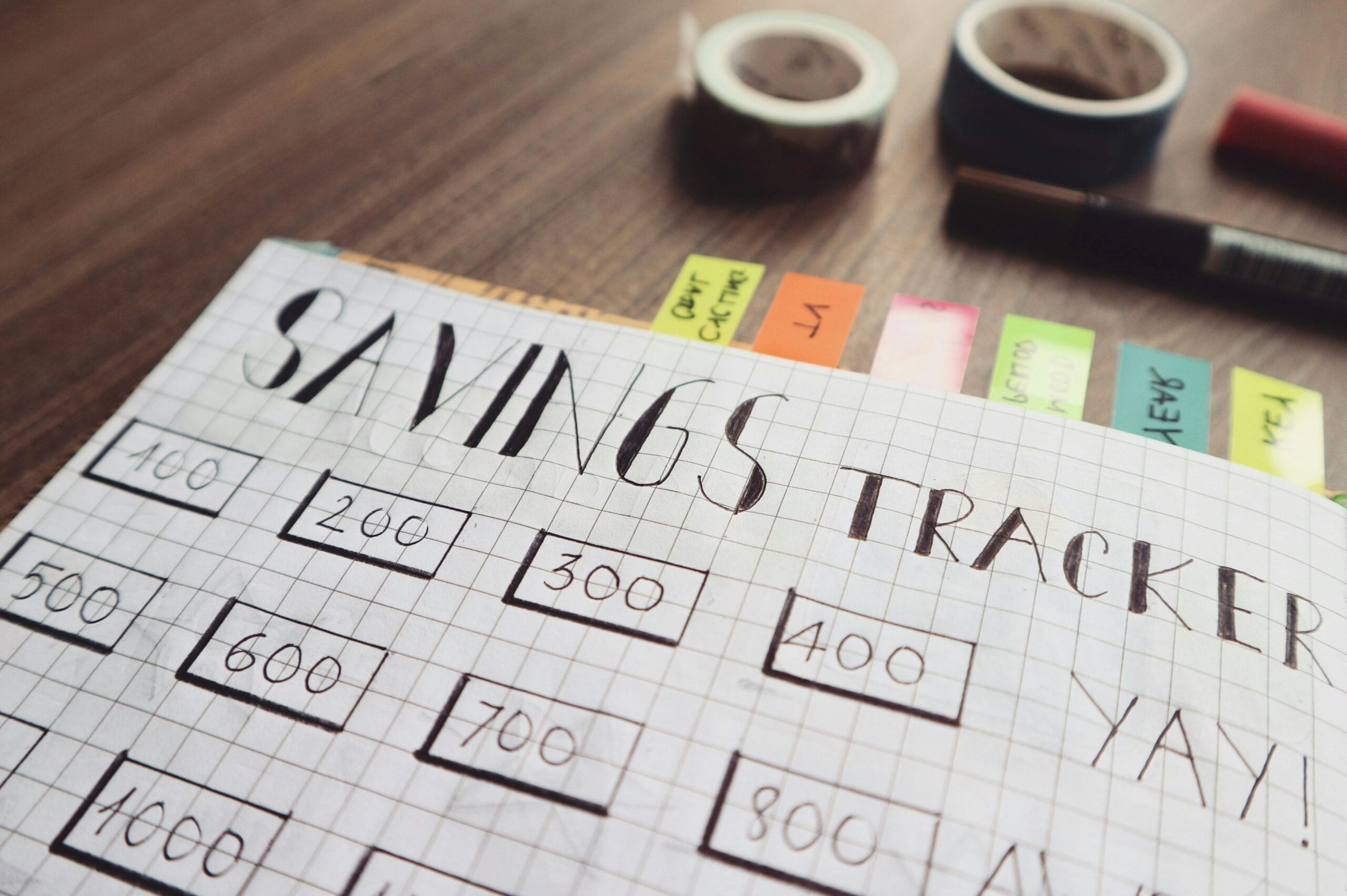 Close-up of a handmade savings tracker with colored tabs on a wooden table, ideal for financial planning visuals and how to set financial goals